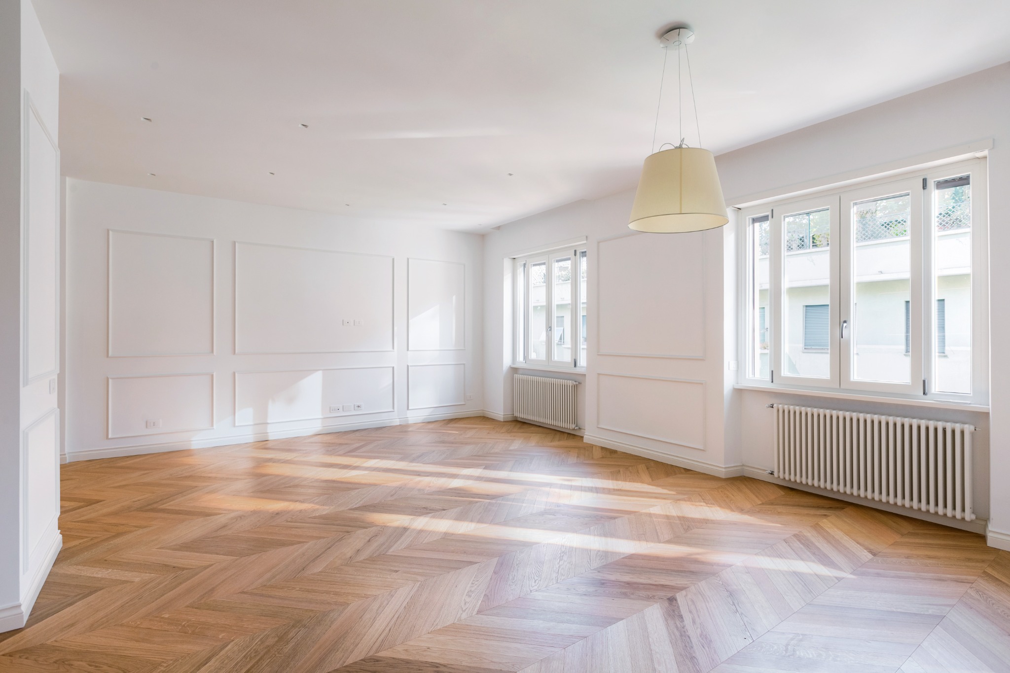 Living luminoso con boiserie bianche, parquet a spina di pesce e ampie finestre
