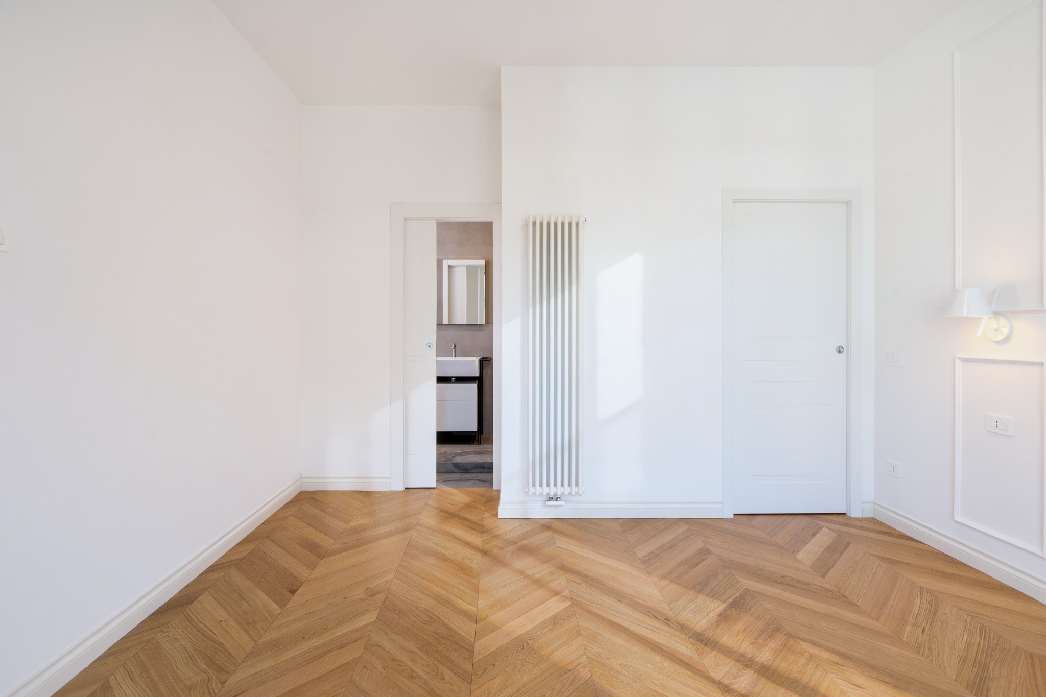 Camera con parquet a spina di pesce, pareti bianche e accesso al bagno